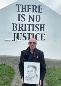 A photograph of Liam Wray standing at Free Derry Corner with a sketch of his brother of Jim Wray, who was killed on Bloody Sunday. 